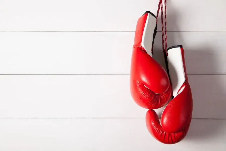 a pair of red and white boxing gloves hung up against a white wooden background